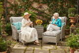 Two women sitting in outdoor furniture with plants and flowers around.
