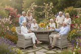 Group of elderly people sitting around a garden table with flowers and plants in the background