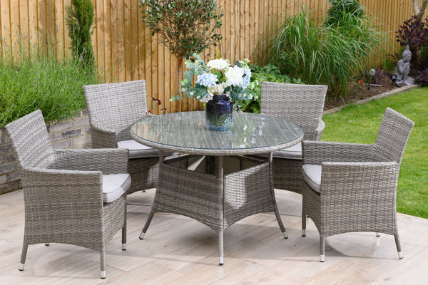 A 4 seater dining set with grey rattan and taupe cushions, consisting of a round table and four chairs, placed on an outdoor patio.