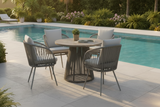 Outdoor patio area with a round table and chairs by a pool, surrounded by greenery.