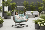 Woman relaxing in a modern outdoor swing chair on a patio with plants and furniture.