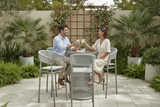 Man and woman sitting at a patio table with drinks, surrounded by plants and outdoor furniture.