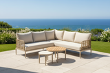 Outdoor patio set with beige cushions and wooden tables on a patio with ocean view