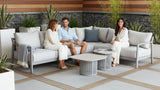 Three people sitting on a modern outdoor sofa set with plants and a wooden wall in the background.