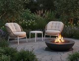 Two cushioned chairs and a small table around a fire pit in a garden setting.
