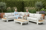 Two elderly people sitting on a modern outdoor sofa set with a wooden coffee table, surrounded by plants.