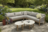 Outdoor patio setting with a sectional sofa, coffee tables, and decorative pillows in a garden.